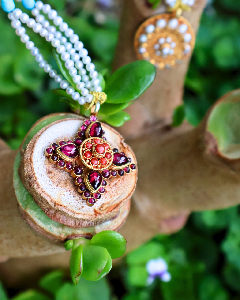 Decorative necklace with red and gold pendant on a wooden block with green leaves in the background