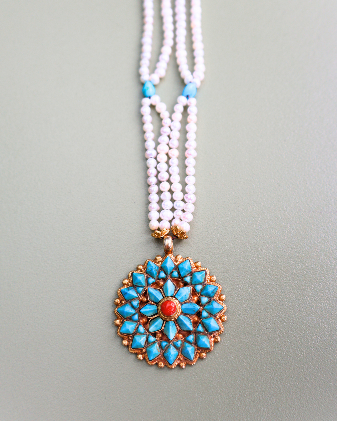 Necklace with a decorative pendant featuring turquoise stones and a red center on a gray background