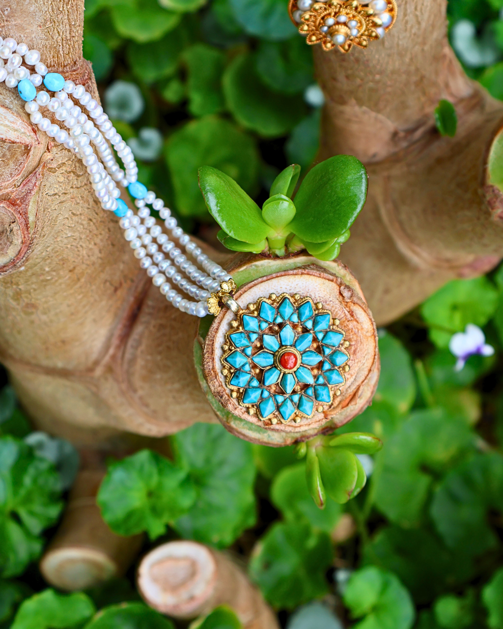 Decorative necklace with turquoise stones and red center on a green leafy background