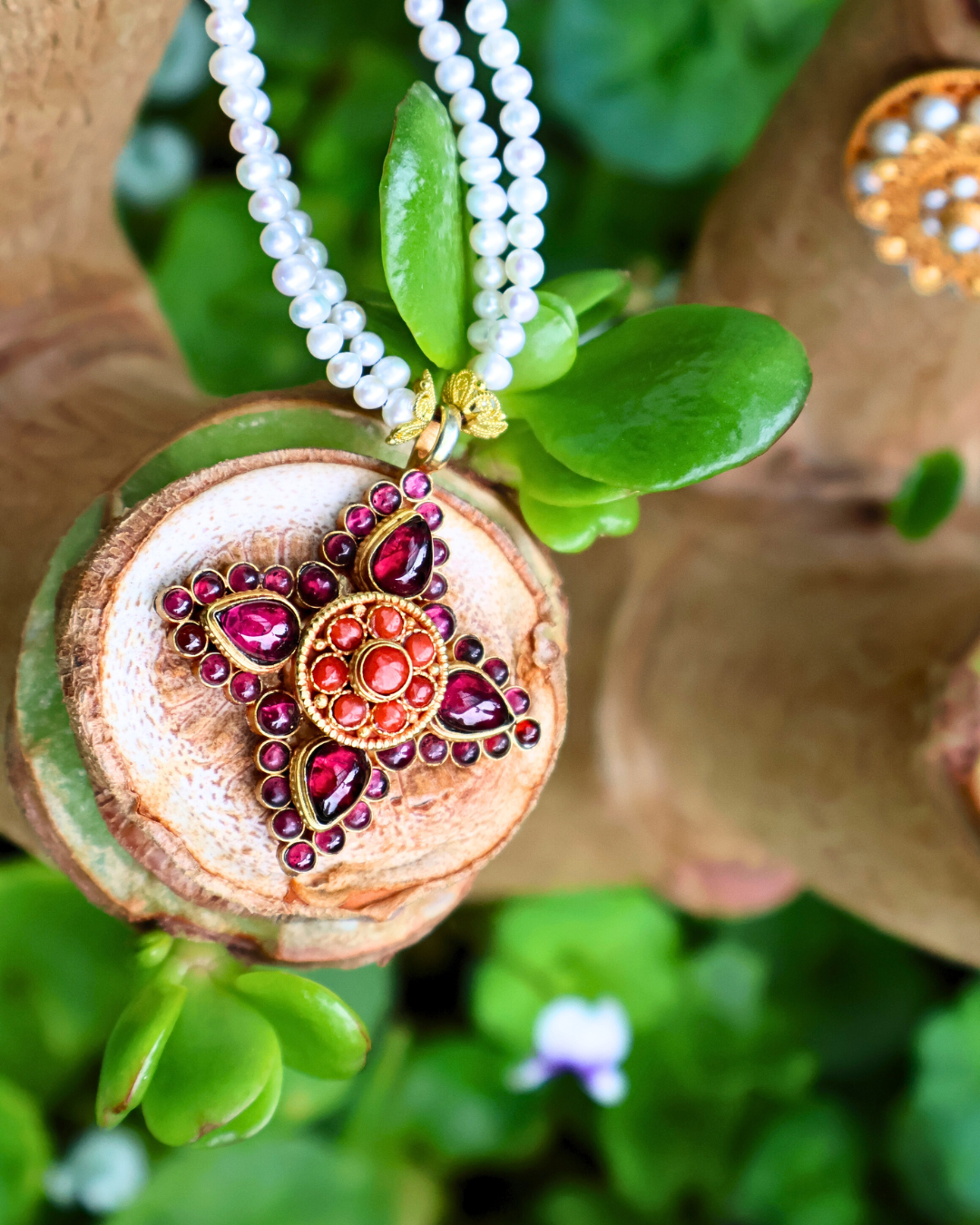 Decorative pendant with red gemstones on a white beaded necklace, set against a natural background.