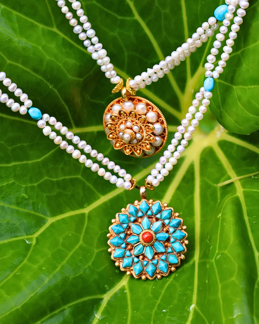 Two pearl necklaces with decorative pendants on a green leaf background