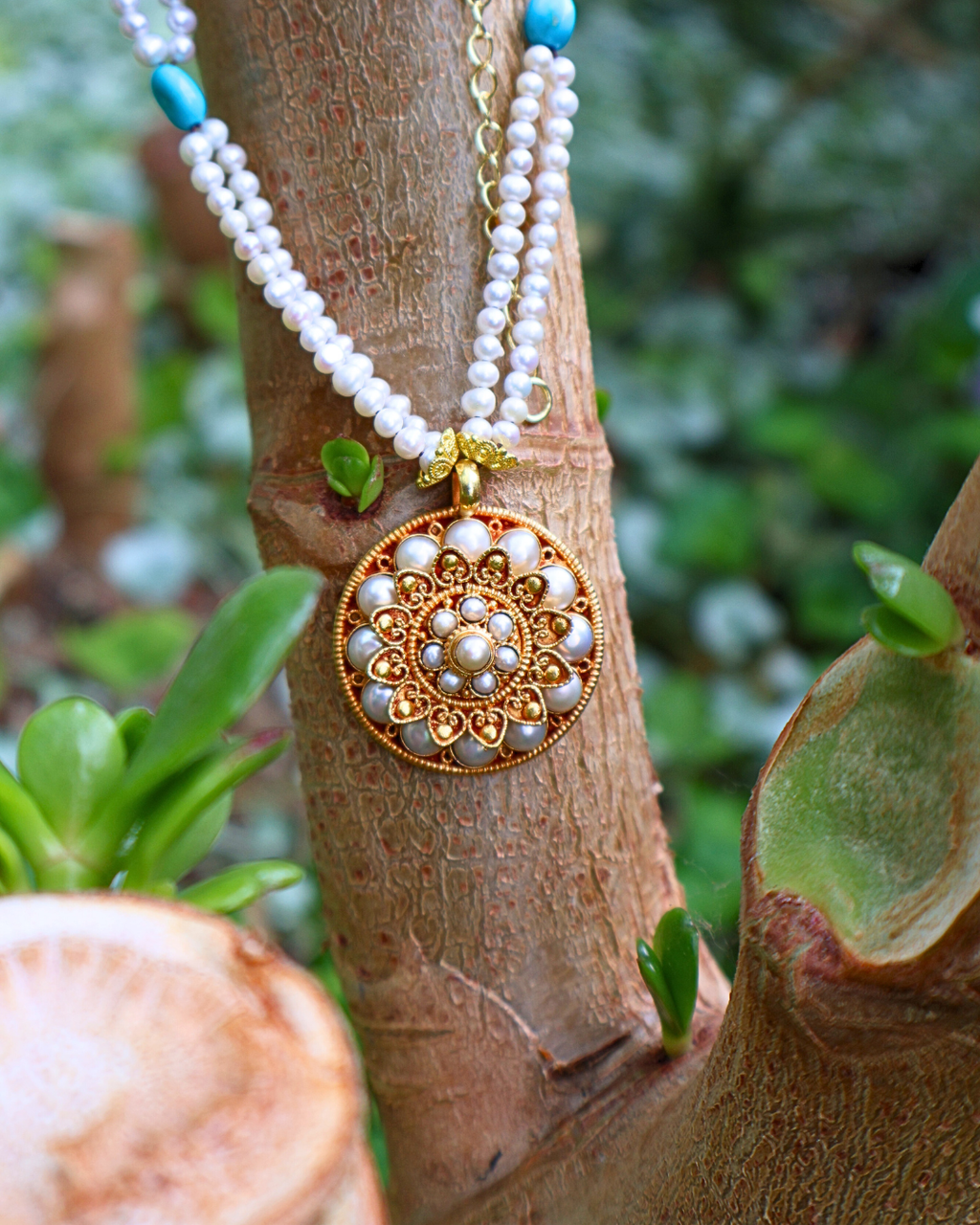 Necklace with a decorative pendant on a wooden branch with green foliage in the background